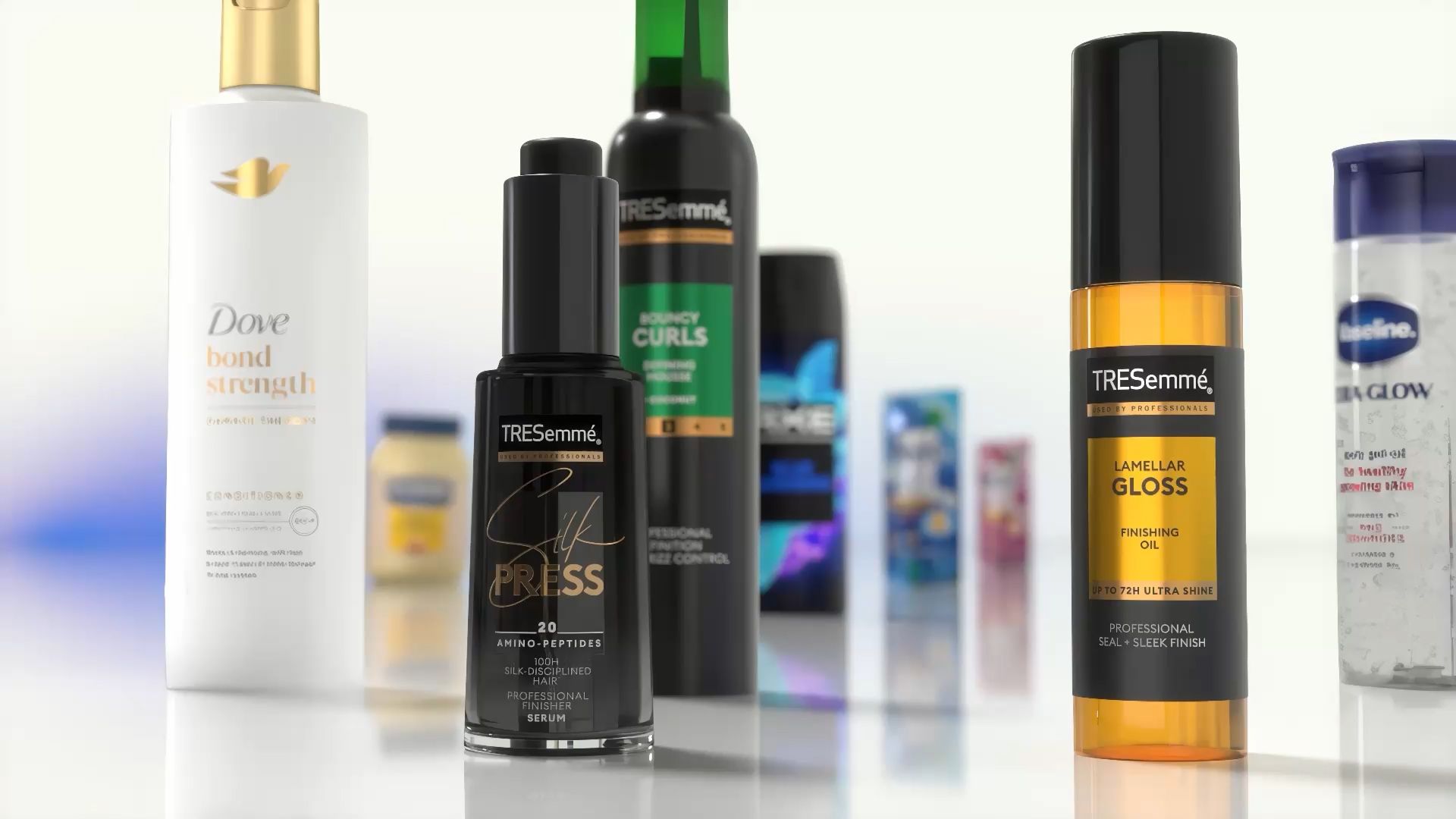 Detailní záběr na různé produkty péče o vlasy a tělo vystavené na reflexní ploše. Mezi viditelnými položkami v pozadí je kondicionér Dove Bond Strength, sérum TRESemmé Silk Press, lak na vlasy TRESemmé Lamellar Gloss a další produkty Unilever.