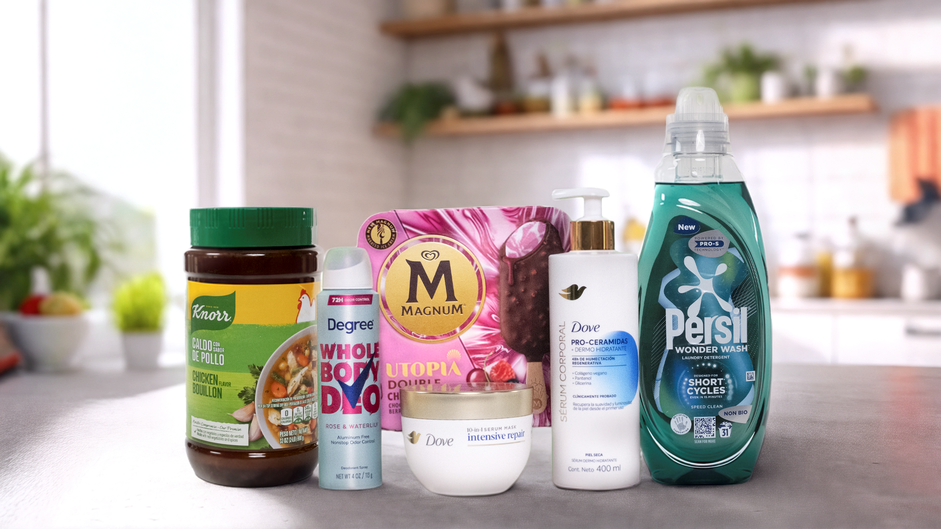 Různé hlavní značky společnosti Unilever uspořádané na kuchyňské lince. Zleva doprava můžete vidět sklenici Knorr kuřecího bujónu, sprej deodorant Degree s nápisem "WHOLE BODY DEO", krabici zmrzliny Magnum s nápisem "UTOPIA", láhev tělového mléka Dove s pro-ceramidovým sérem, sklenici krému Dove Intensive Repair a láhev pracího prostředku Persil Wonder Wash. V pozadí je moderní kuchyně s rostlinami a různými předměty na policích.